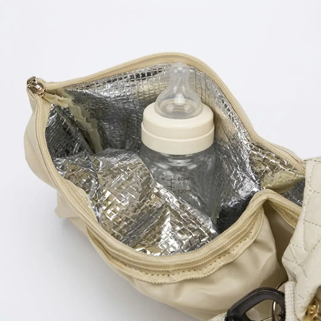  Gros plan sur une poche isotherme ouverte d'un sac à langer, biberon posé à l'intérieur, doublure aluminisée réfléchissante visible, fond blanc.