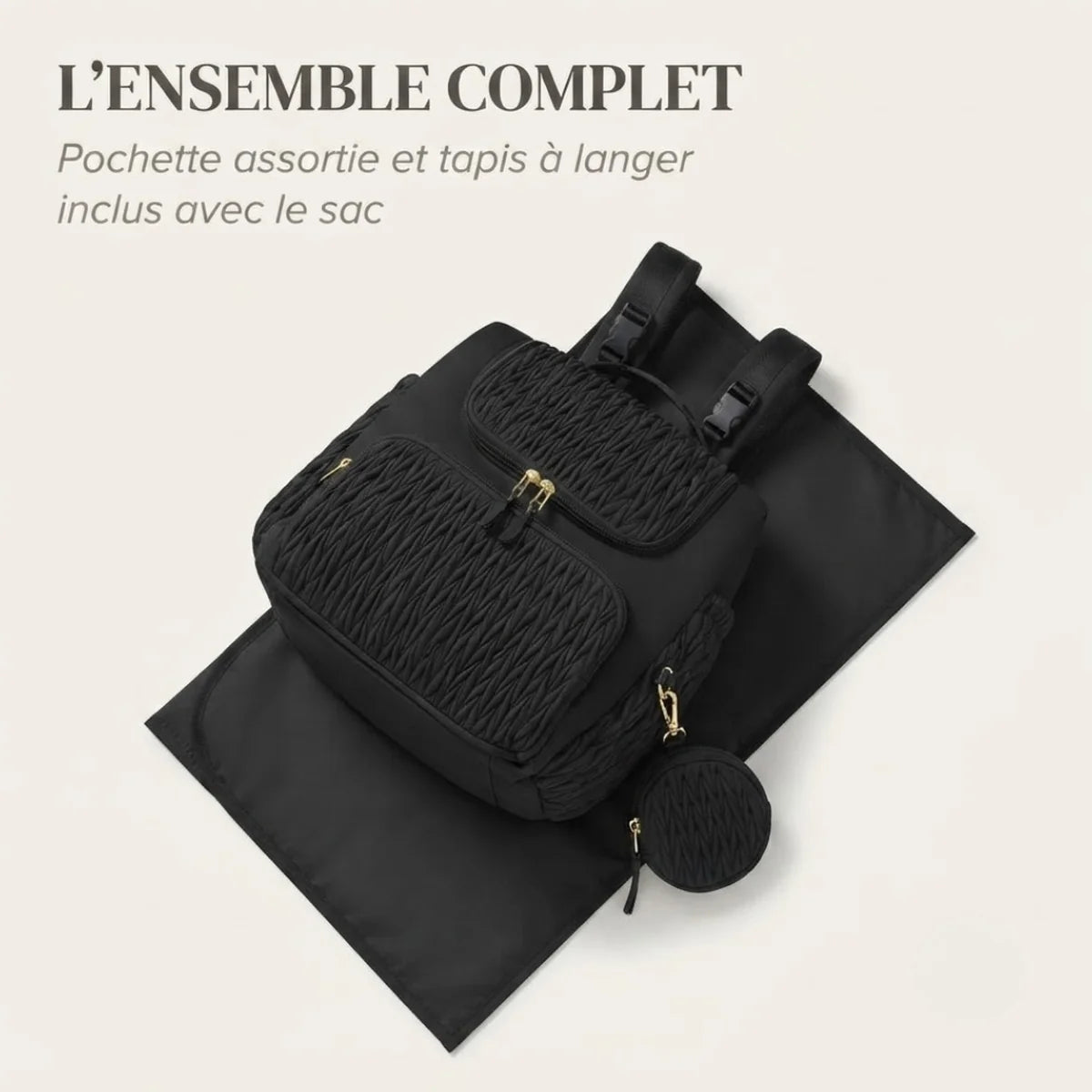 Mise en scène du sac à langer à poches isothermes avec le tapis à langer déplié en dessous et la pochette ronde assortie posée à côté, fond crème.