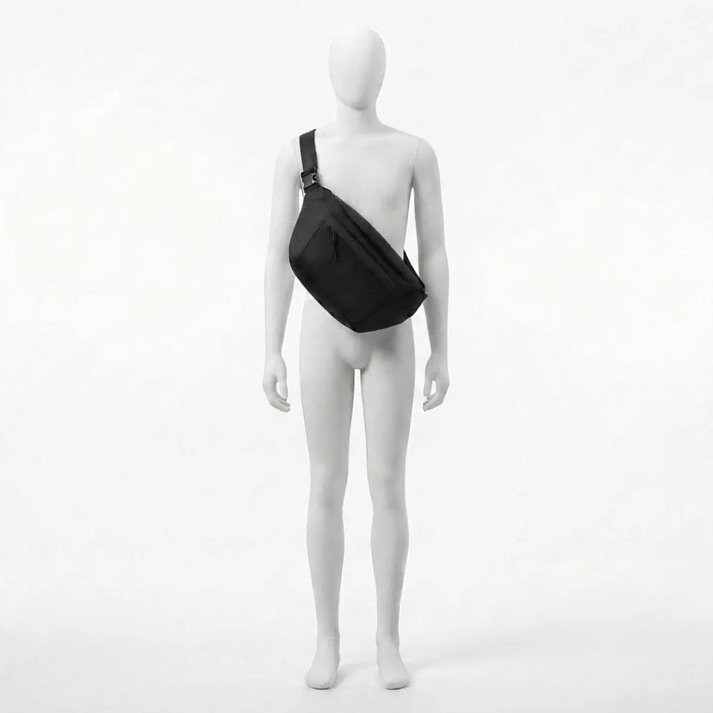 Vue du sac banane à langer grand format porté par le mannequin, sangle passant de l'épaule à la hanche opposée, boucle de réglage visible au niveau de l'épaule.